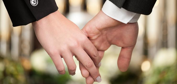 Hände eines Paares halten sich, im Hintergrund verschwommene Kerzen und florale Dekorationen.